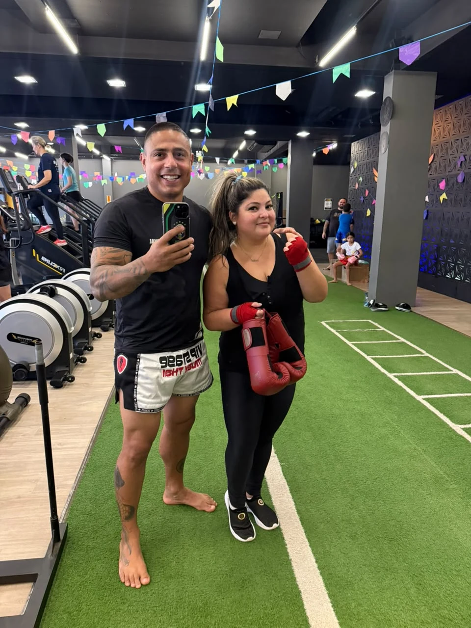 Anderson Hickman e aluna com luvas de treino na área funcional