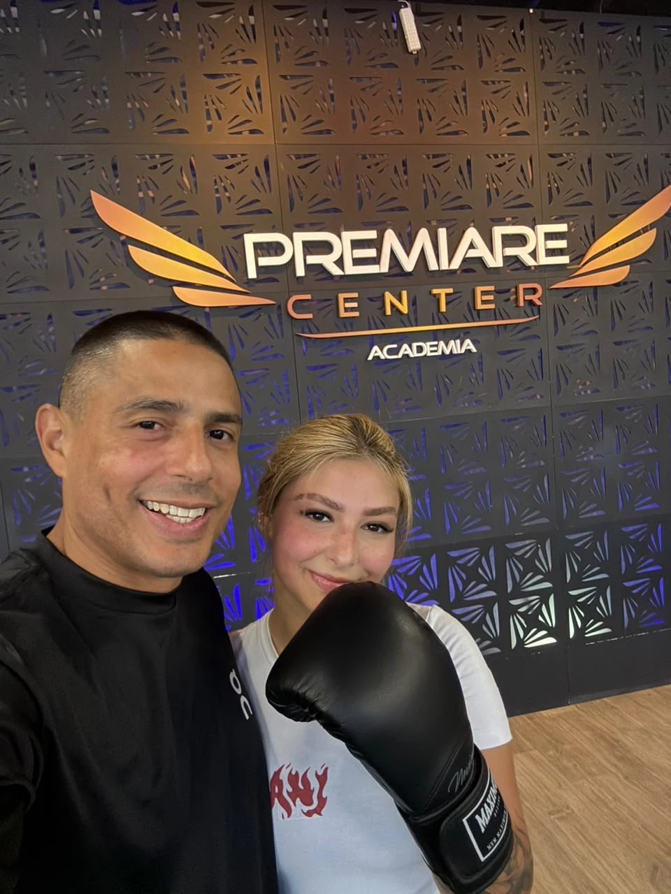 Anderson Hickman e aluna com luva de boxe diante do painel da Premiare Center